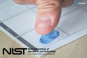 Primer plano de un dedo pulgar dejando una huella dactilar con tinta azul en un formulario oficial de papel blanco, con el logotipo de NIST y la marca de agua de Ver&aacute;zial.